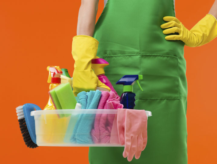 Close-up of cleaning lady holding supplies, on orange background