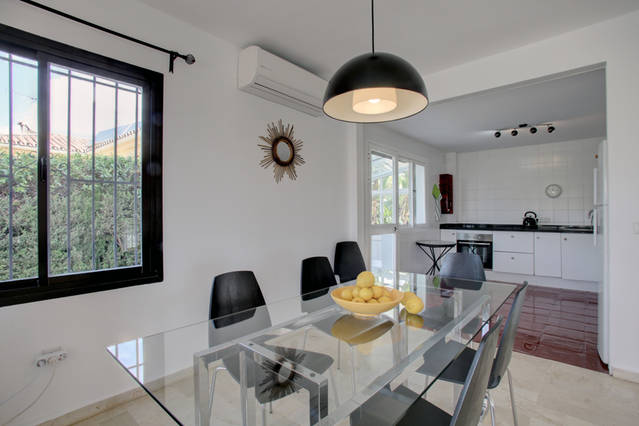 Image shows dining are with large glass table and view into kitchen