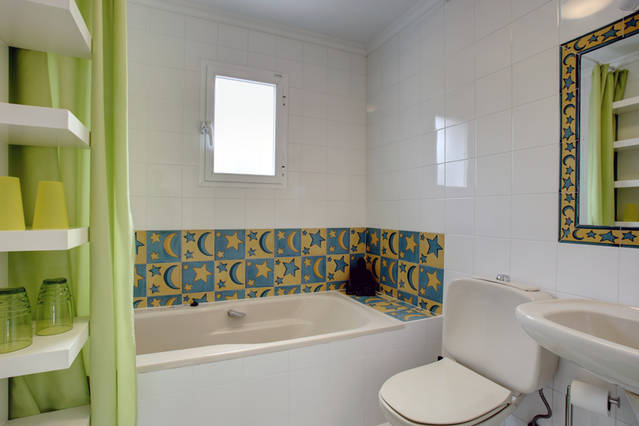 Image shows second bathroom with full bath suite, shelving with curtain and tiles with coloured splashback and matching mirror