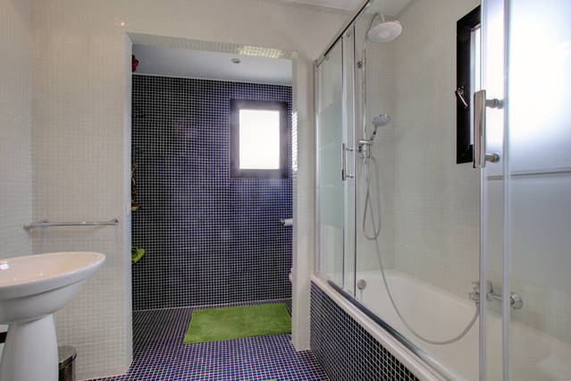 Image shows main bathroom with bath and shower attachment. Tiled floor and walls in wetroom style