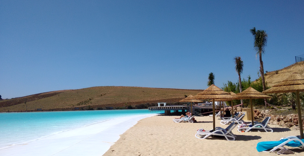 Image shows crystal lagoon with white sand and sunloungers and umbrellas