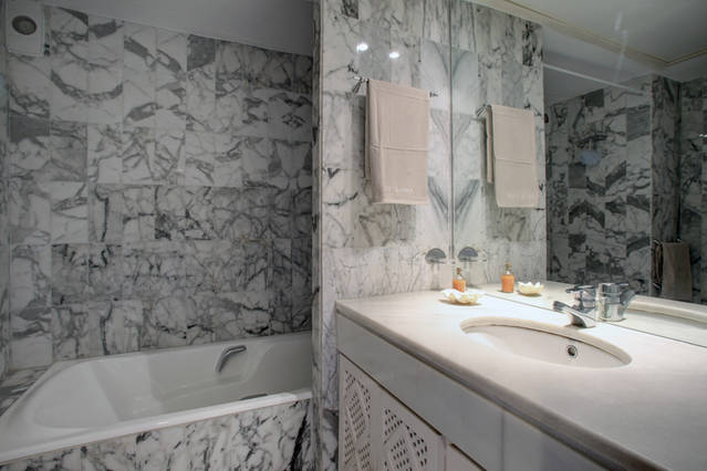 Image shows large marble bathroom with a bath and shower
