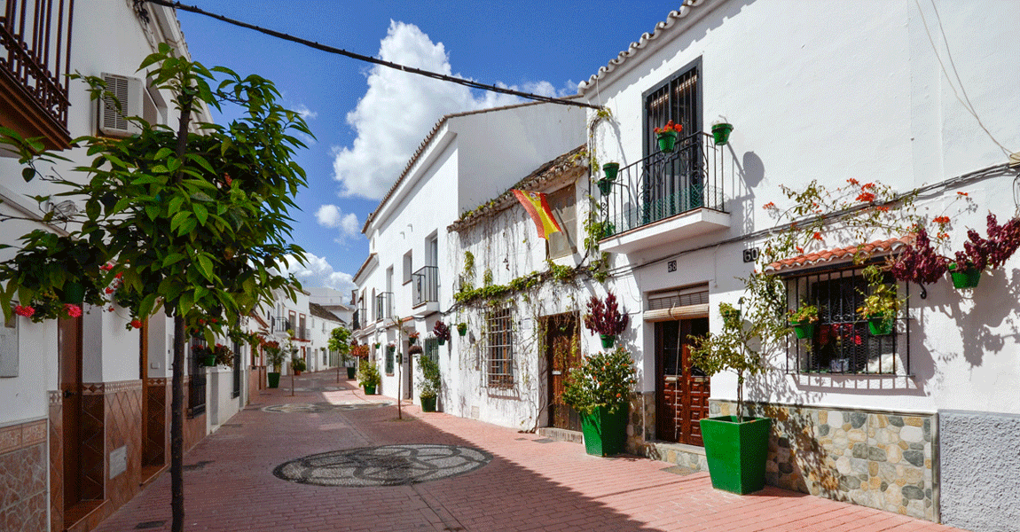 Image shows a street in the old town with traditional cobbles and decorations as well as plants, trees and whitewashed houses - part of the Estepona attractions and activities