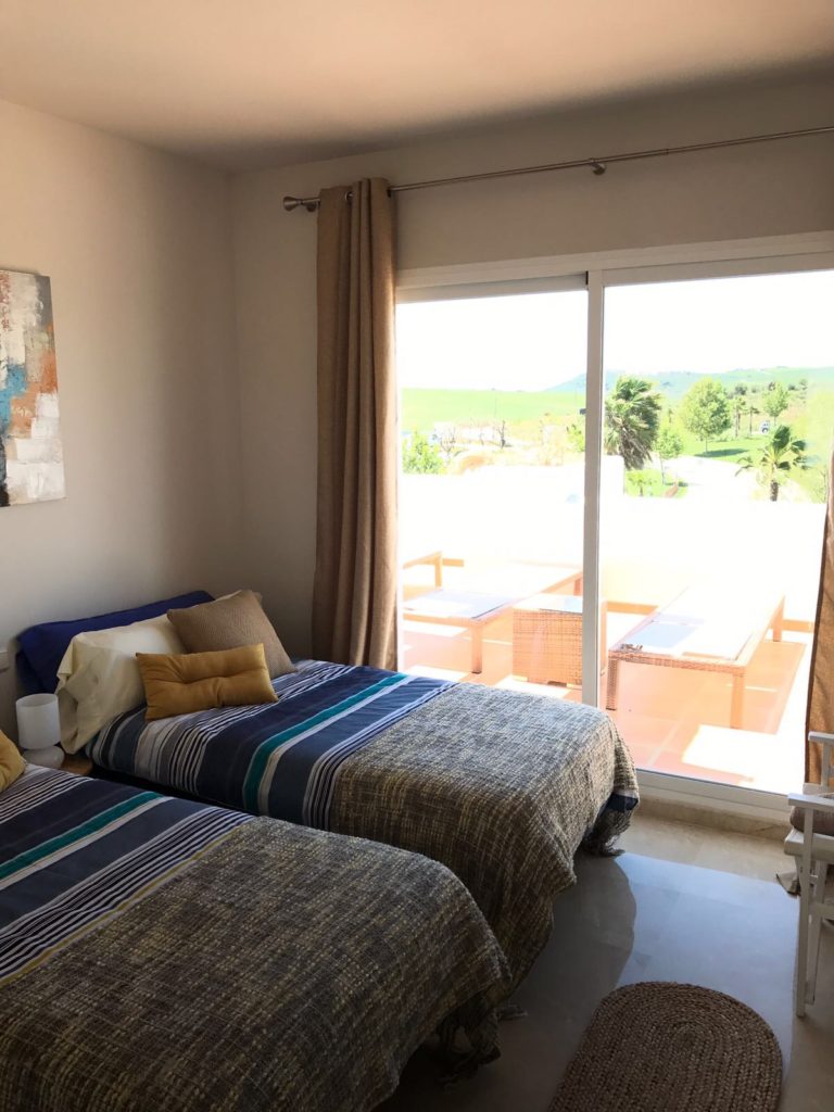 Image shows second bedroom with twin beds and access to the terrace of this stylish penthouse in Alcazaba Lagoon